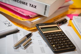 a photo of a messy assortment of papers, books, a pen, and a calculator