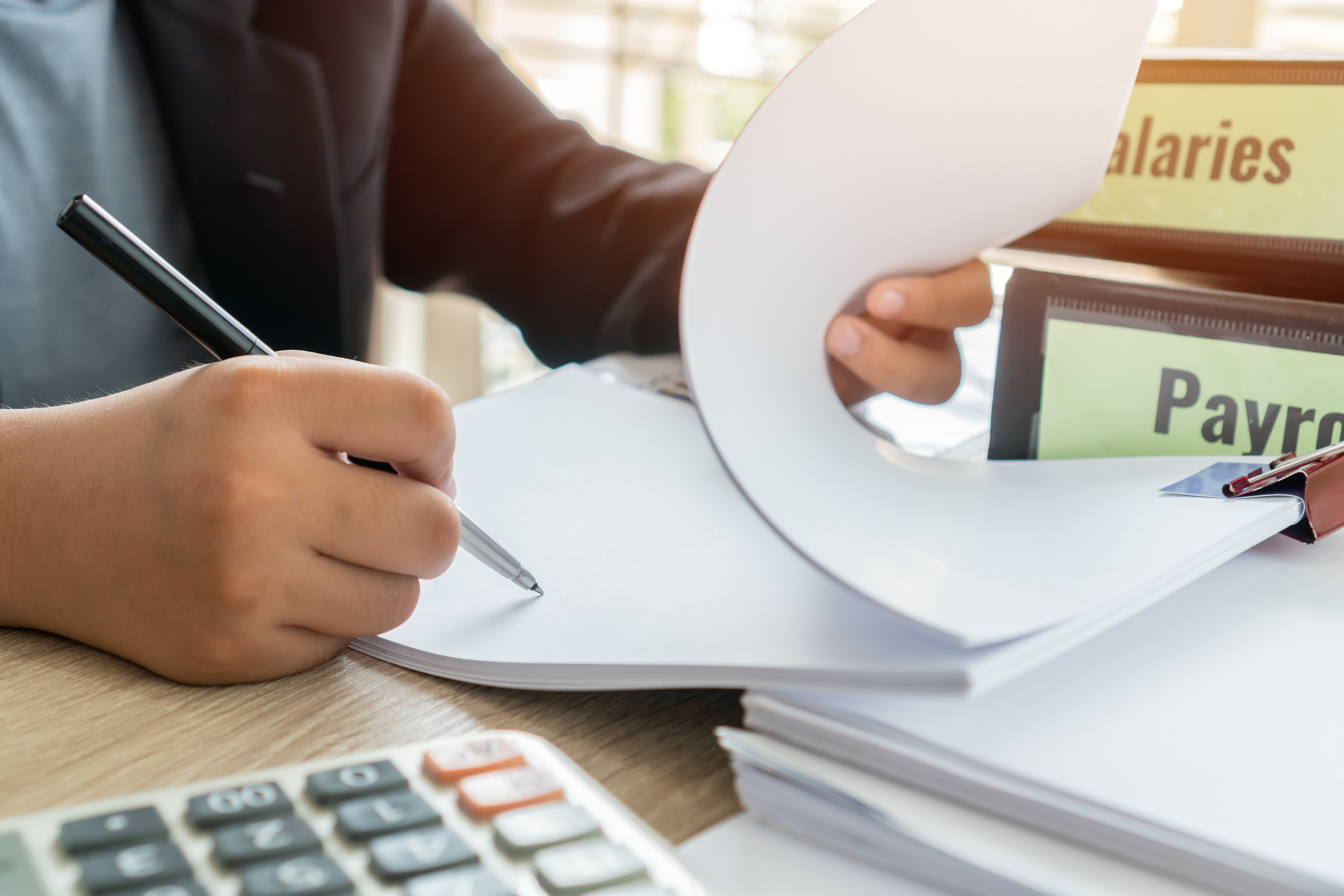 Document report or business management concept: Businessman manager hands holding pen for reading, signing paperwork near payroll salary binder, summary report HR-human resources business bookkeeping