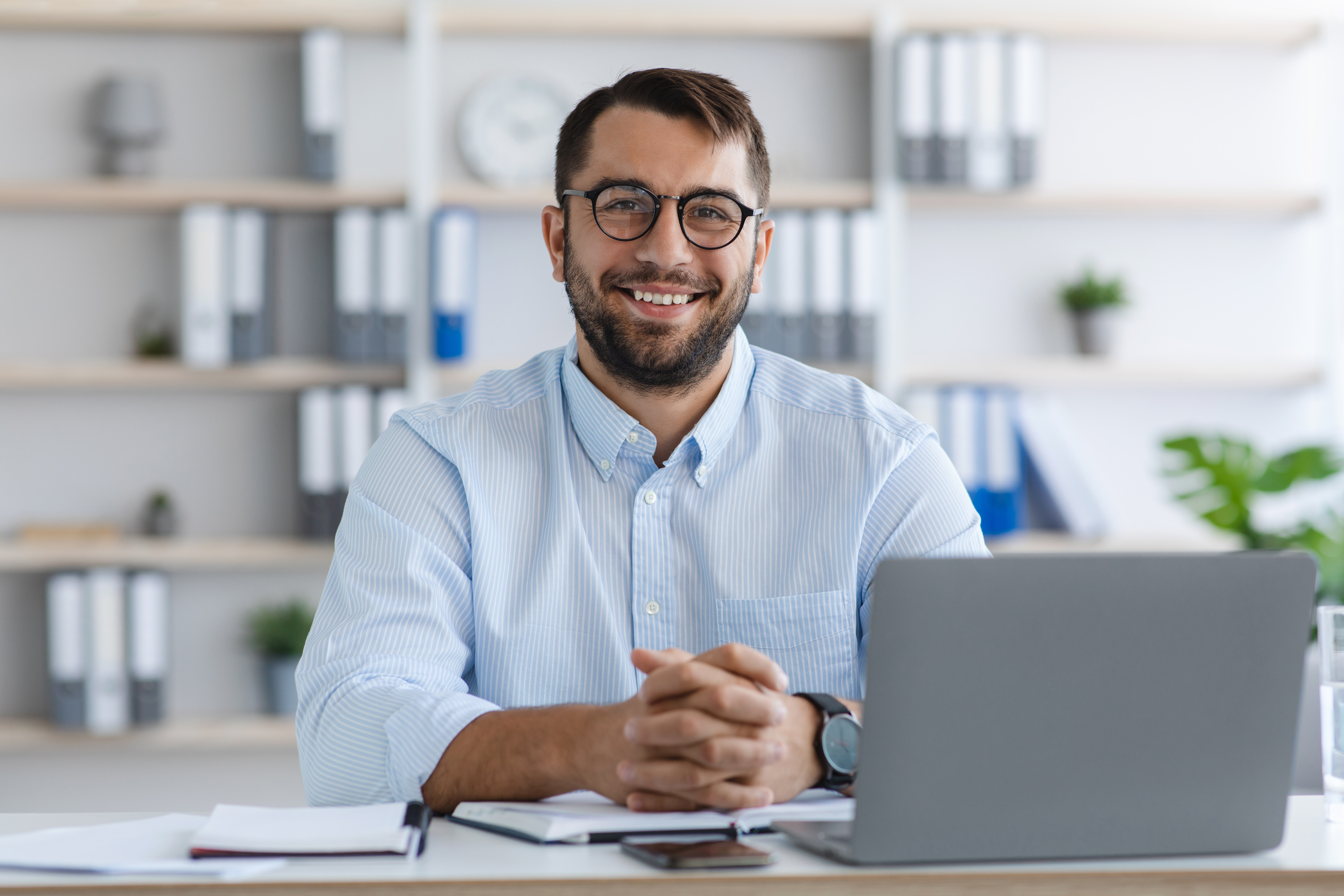 Happy middle aged caucasian man with beard in glasses working with laptop in office or flat interior