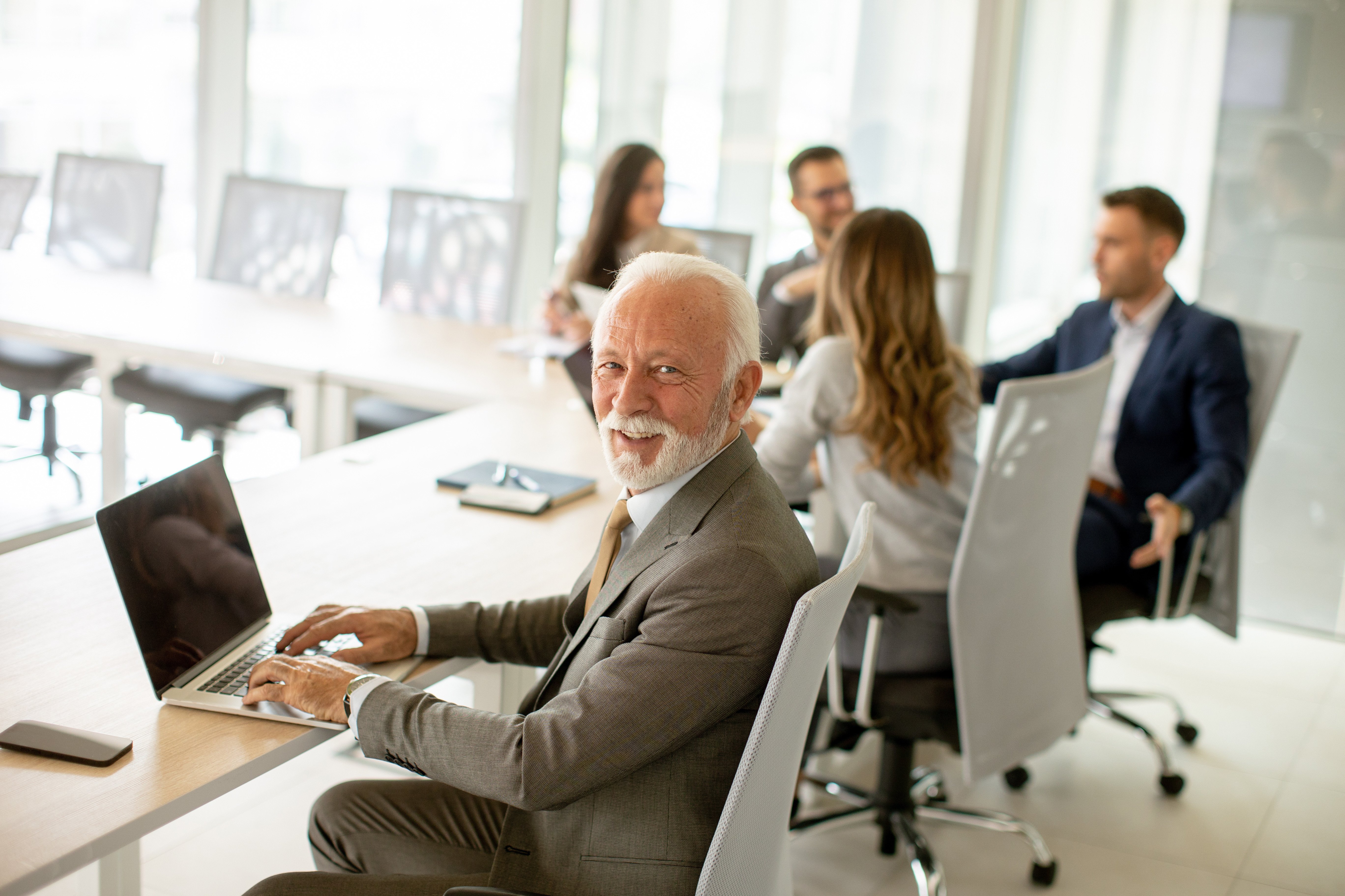 Older man on his computer at a business meeting turned around looking at camera